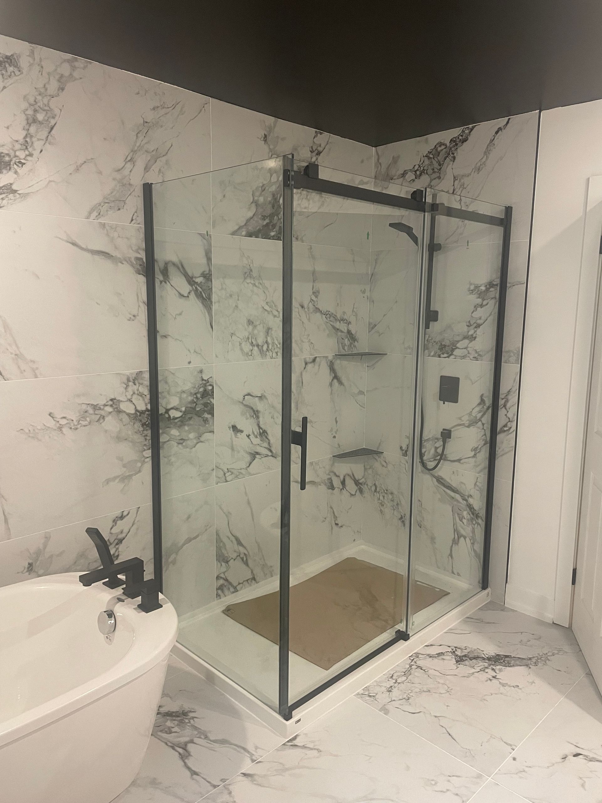 Salle de bains moderne avec une cabine de douche en verre et un mur carrelé à motif marbre blanc.