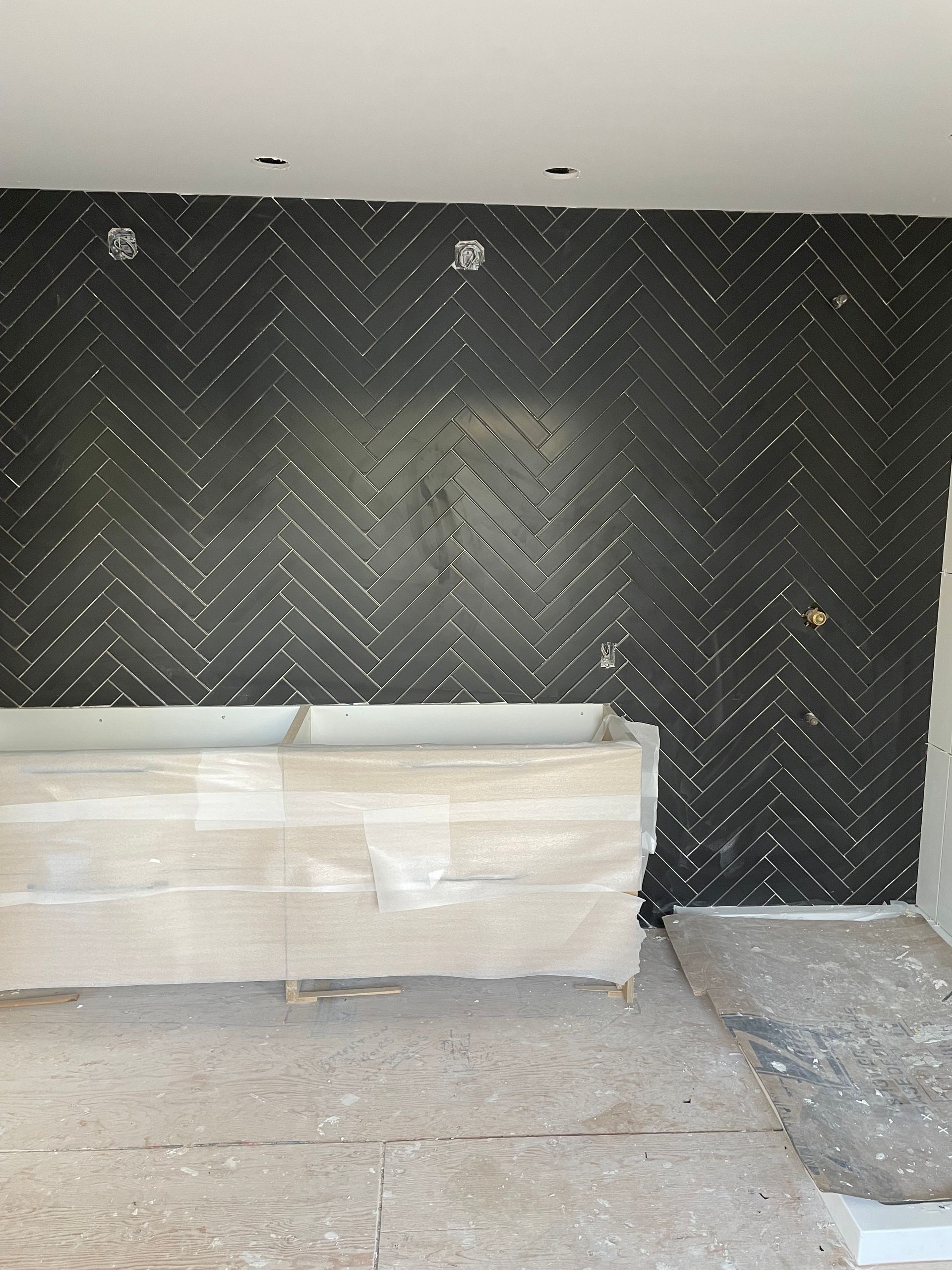 Mur carrelé de carreaux noirs à chevrons, plan de travail clair. Sol en béton brut.