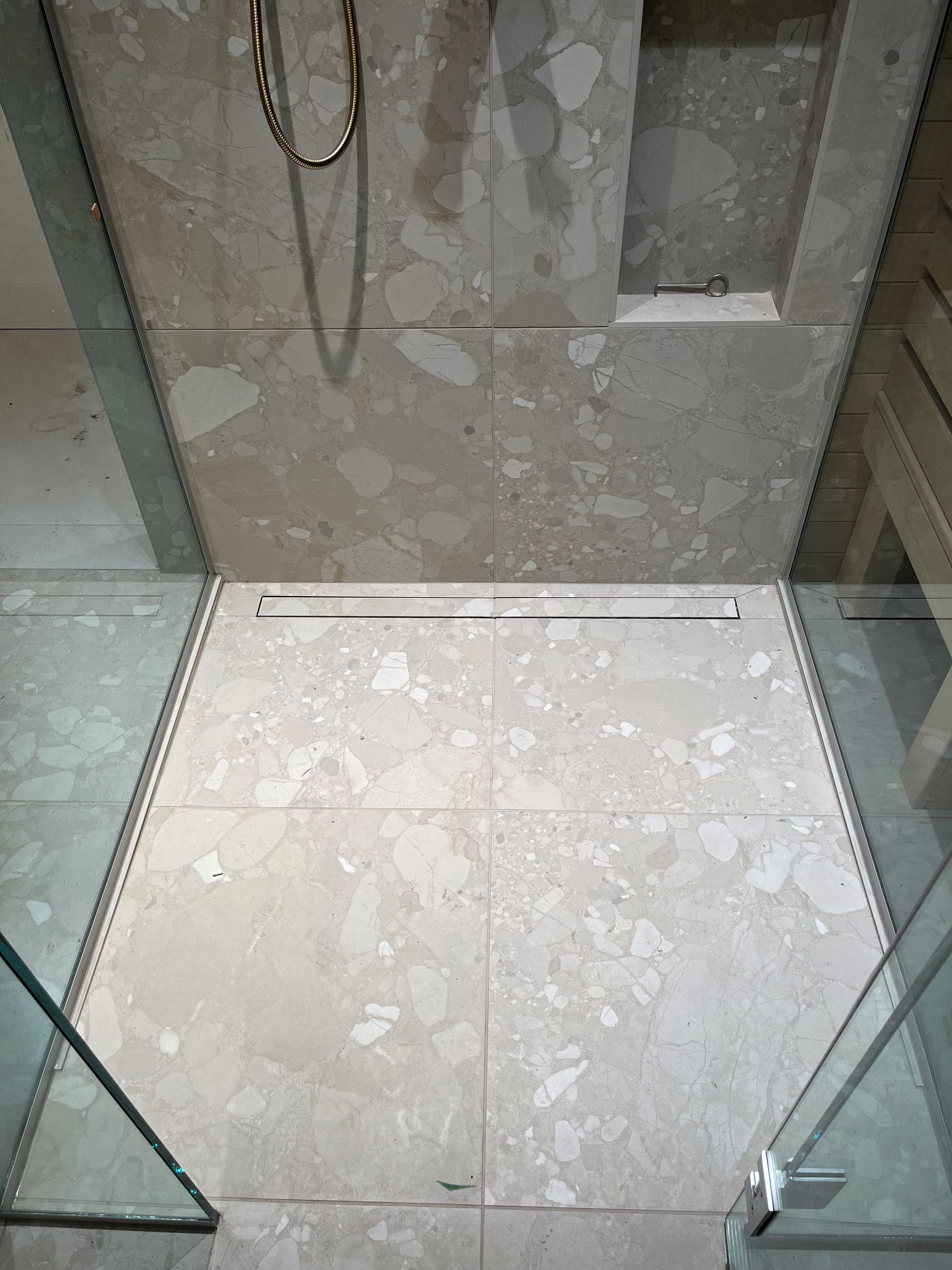 Douche avec grands carreaux beiges, caniveau linéaire et portes en verre.