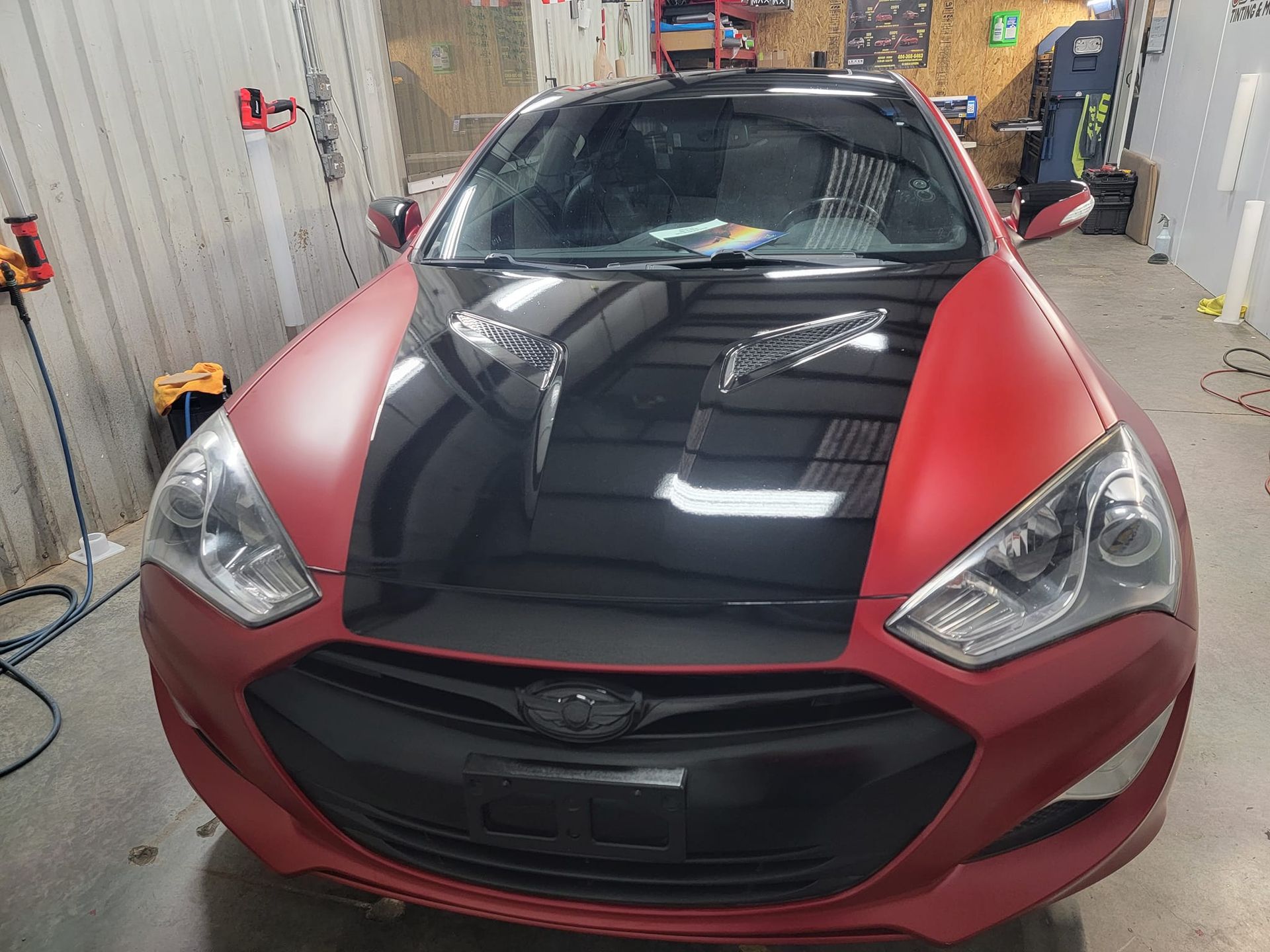 A red car with a black hood is parked in a garage.