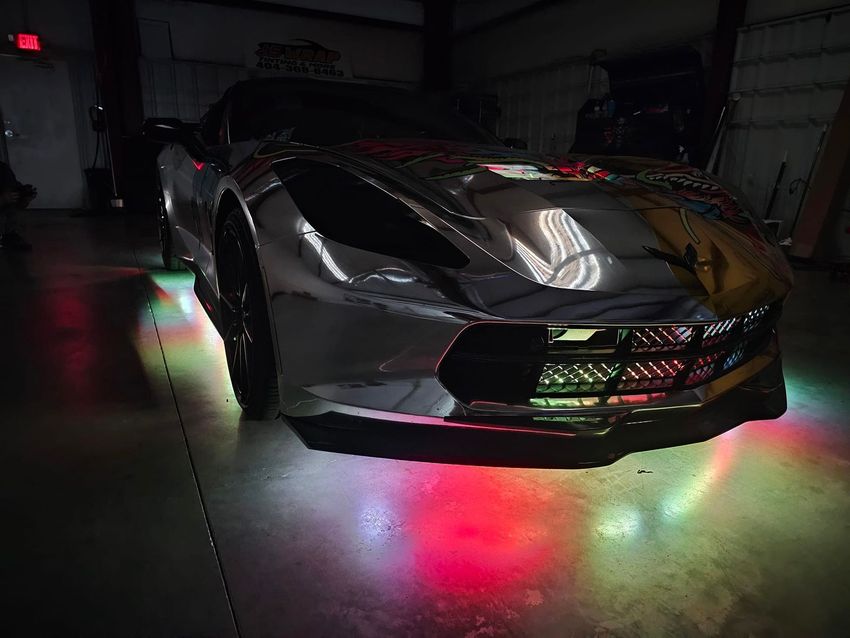 A silver sports car is parked in a garage with colorful lights.
