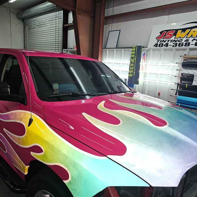 A pink truck with flames painted on the hood