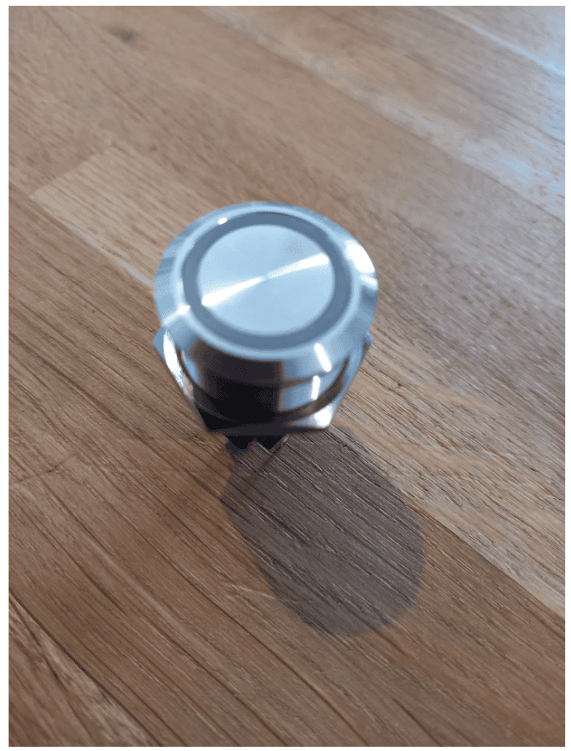 A stainless steel button is sitting on a wooden table.