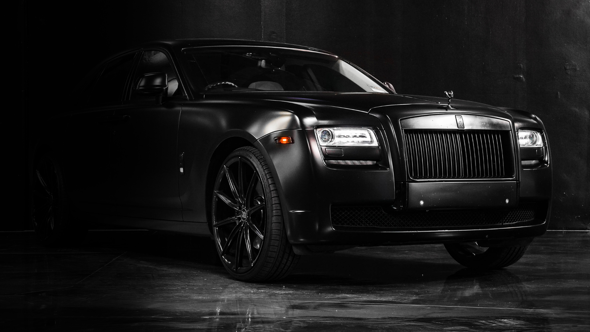 A black rolls royce ghost is parked in a dark room.