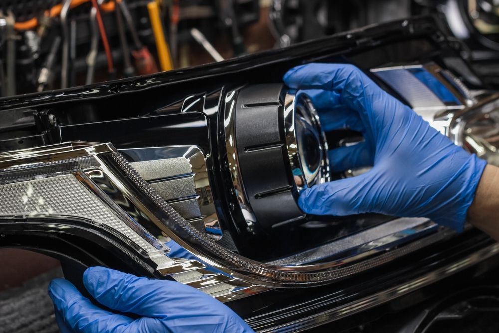 A person wearing blue gloves is working on a car headlight.