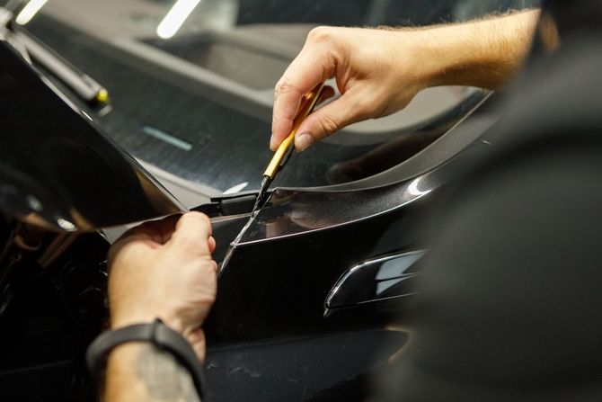 A man is applying a protective film to the windshield of a car.
