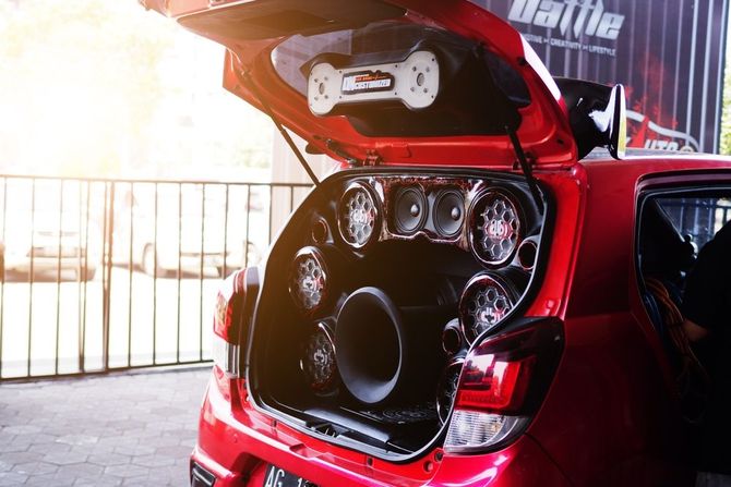 The trunk of a red car with a lot of speakers in it.