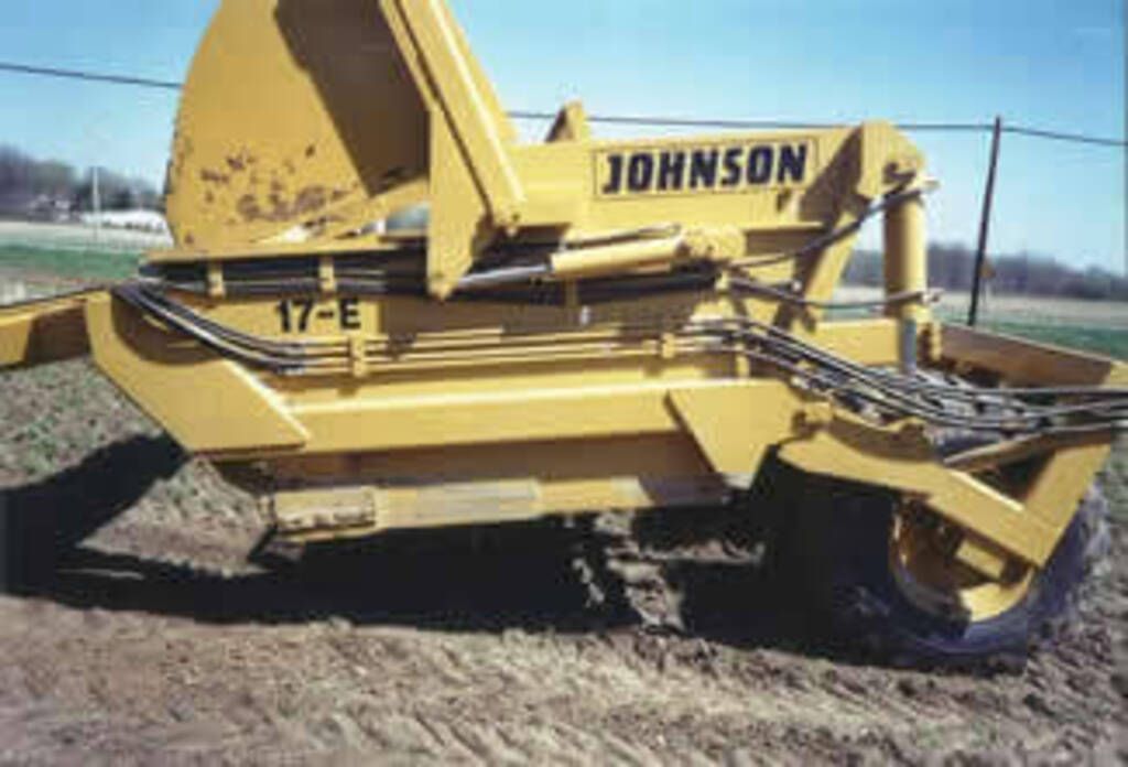 A yellow johnson tractor is parked in a dirt field.