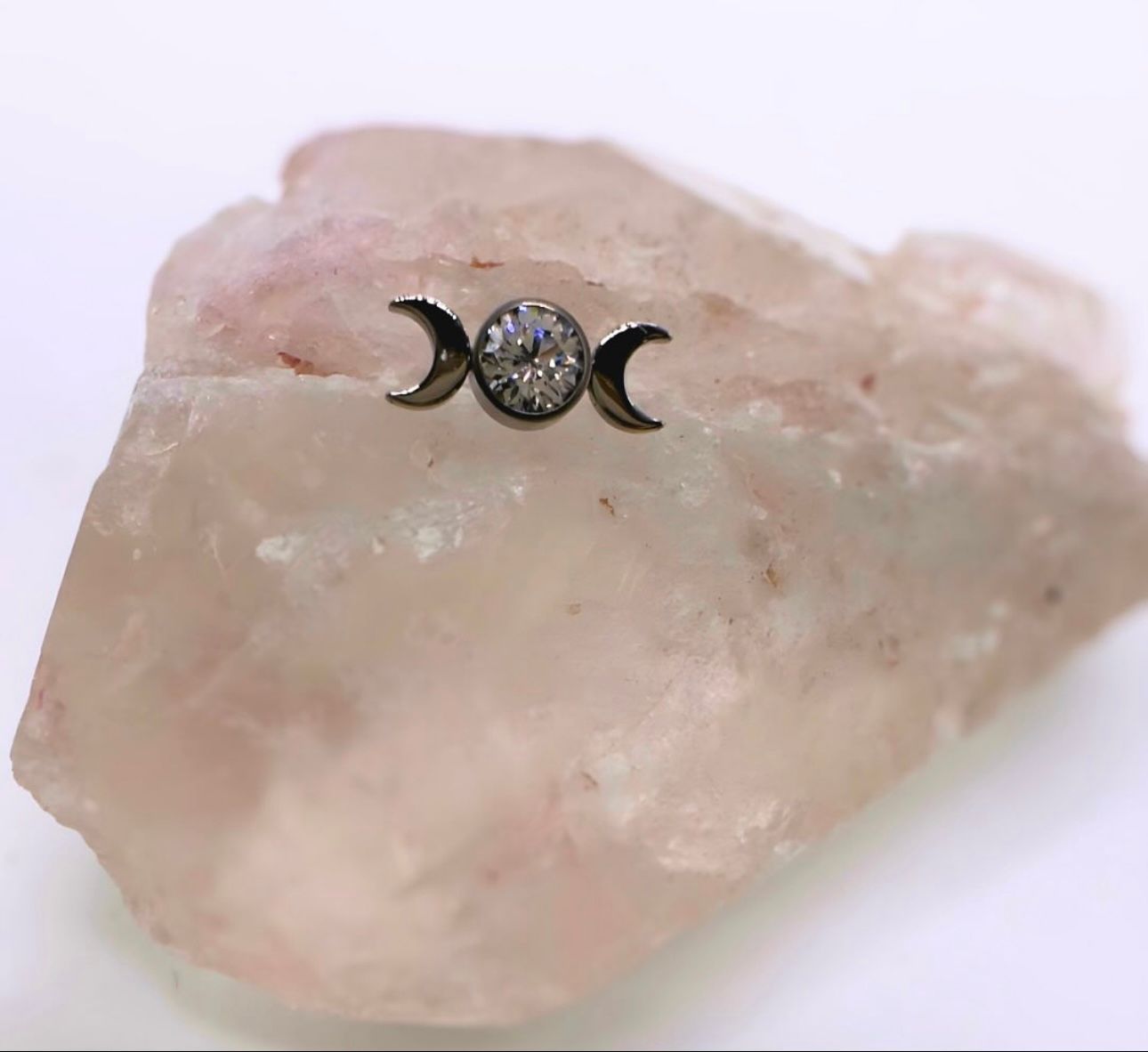 A crescent moon earring is sitting on top of a piece of rock.