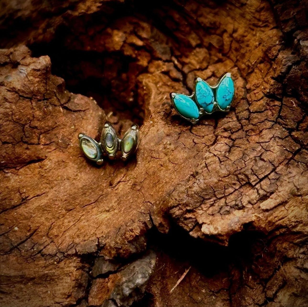 A pair of turquoise stud earrings are sitting on top of a piece of wood.