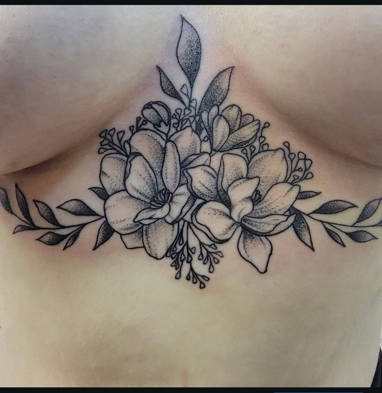 A black and white tattoo of flowers and leaves on a woman 's chest