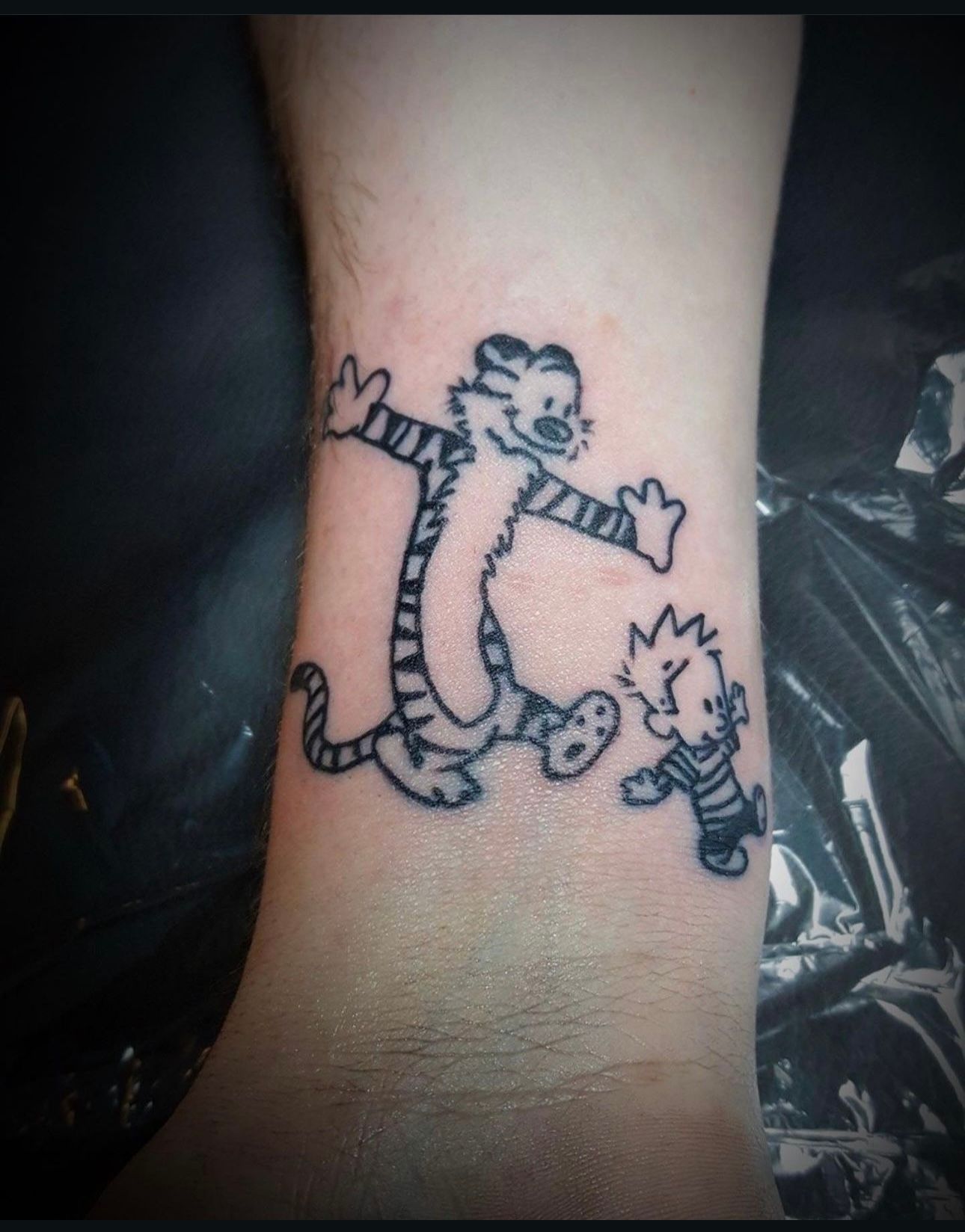A person has a tattoo of calvin and hobbes on their wrist