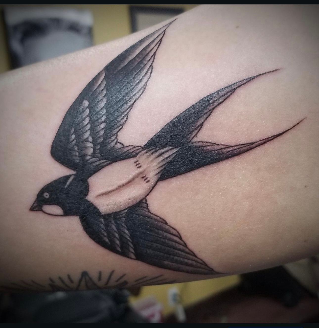A black and white tattoo of a bird on a person 's arm