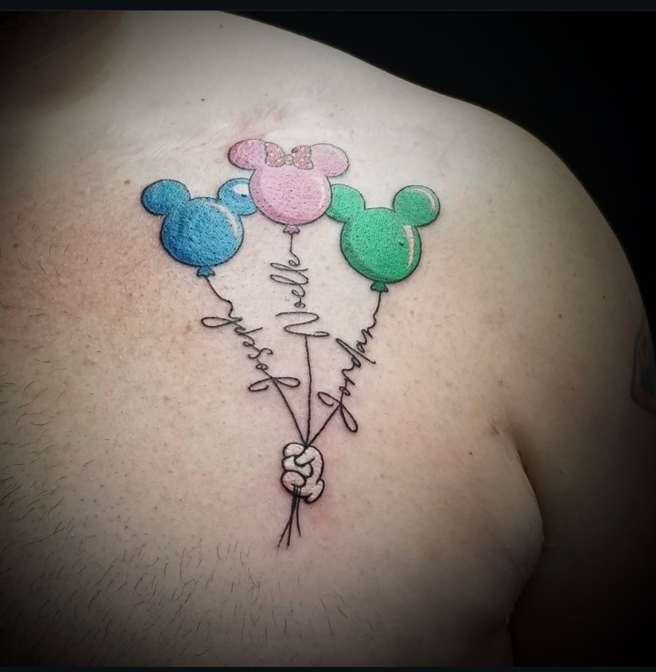A person has a tattoo of mickey mouse balloons on their back