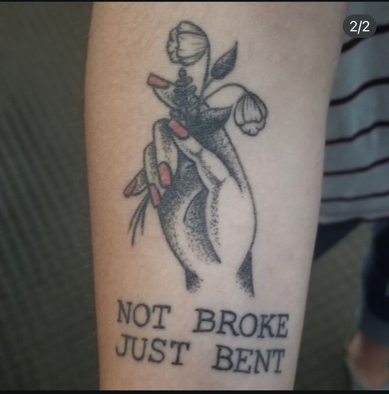 A tattoo of a hand holding a flower that says not broke just bent