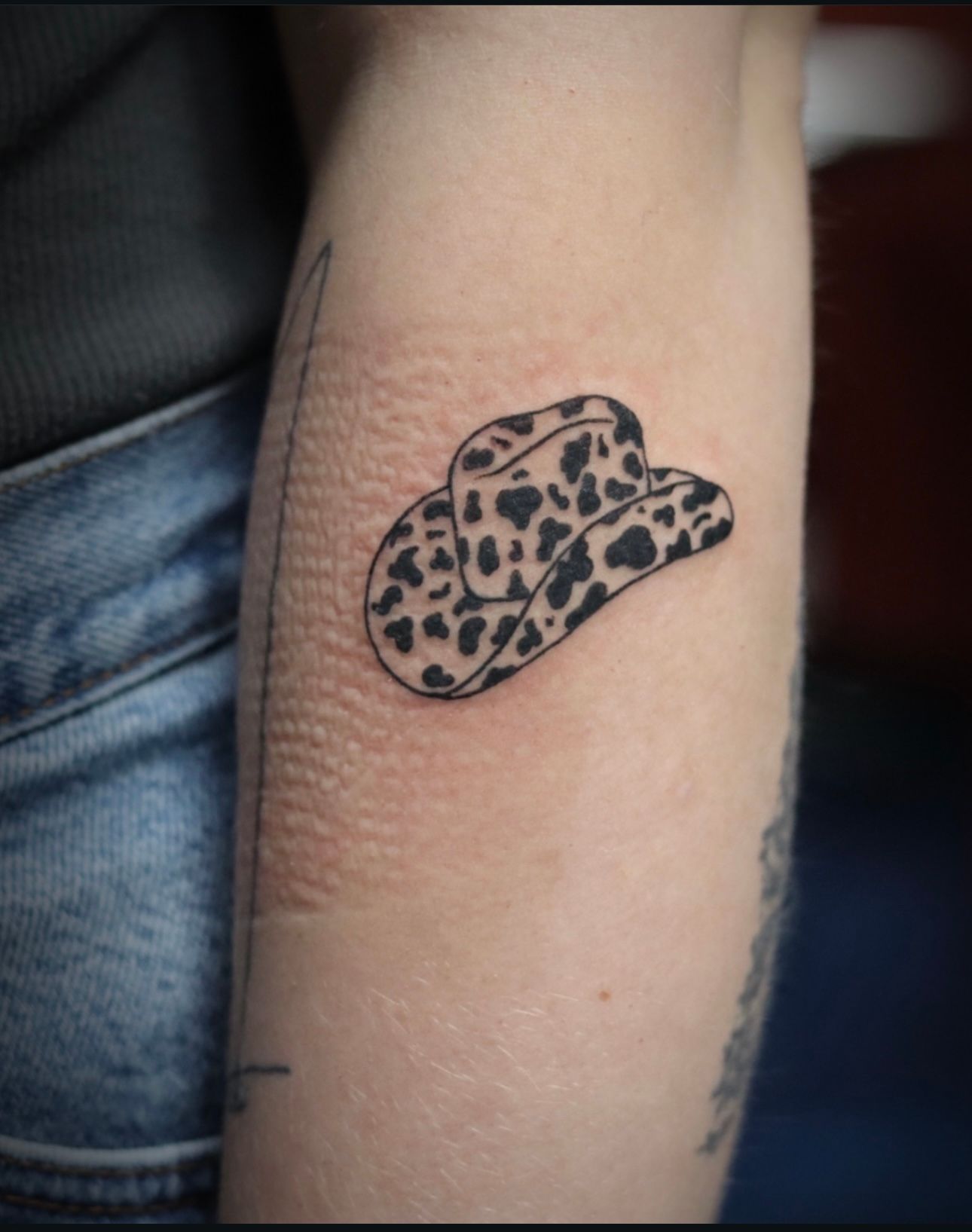 A person has a tattoo of a cowboy hat on their arm