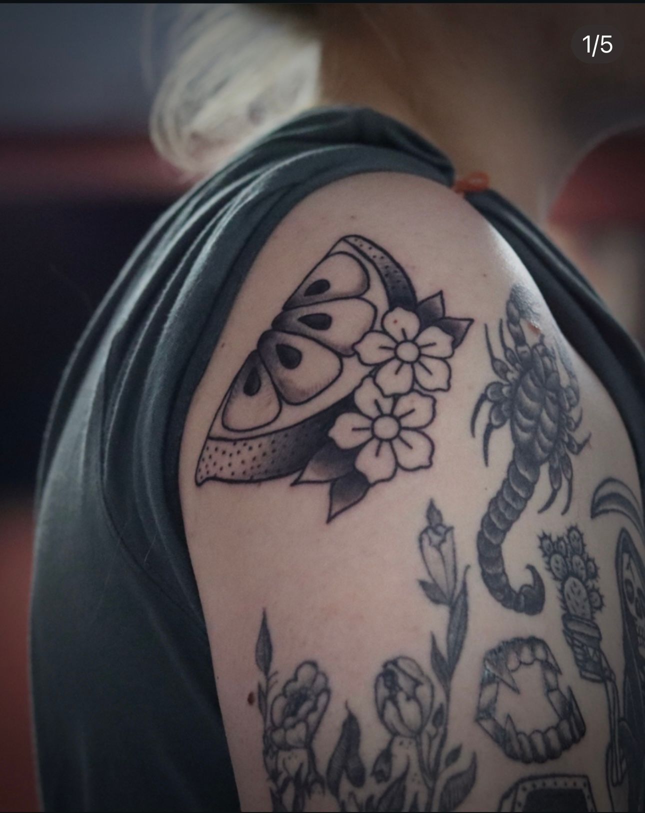 A woman has many tattoos on her arm including a scorpion and flowers