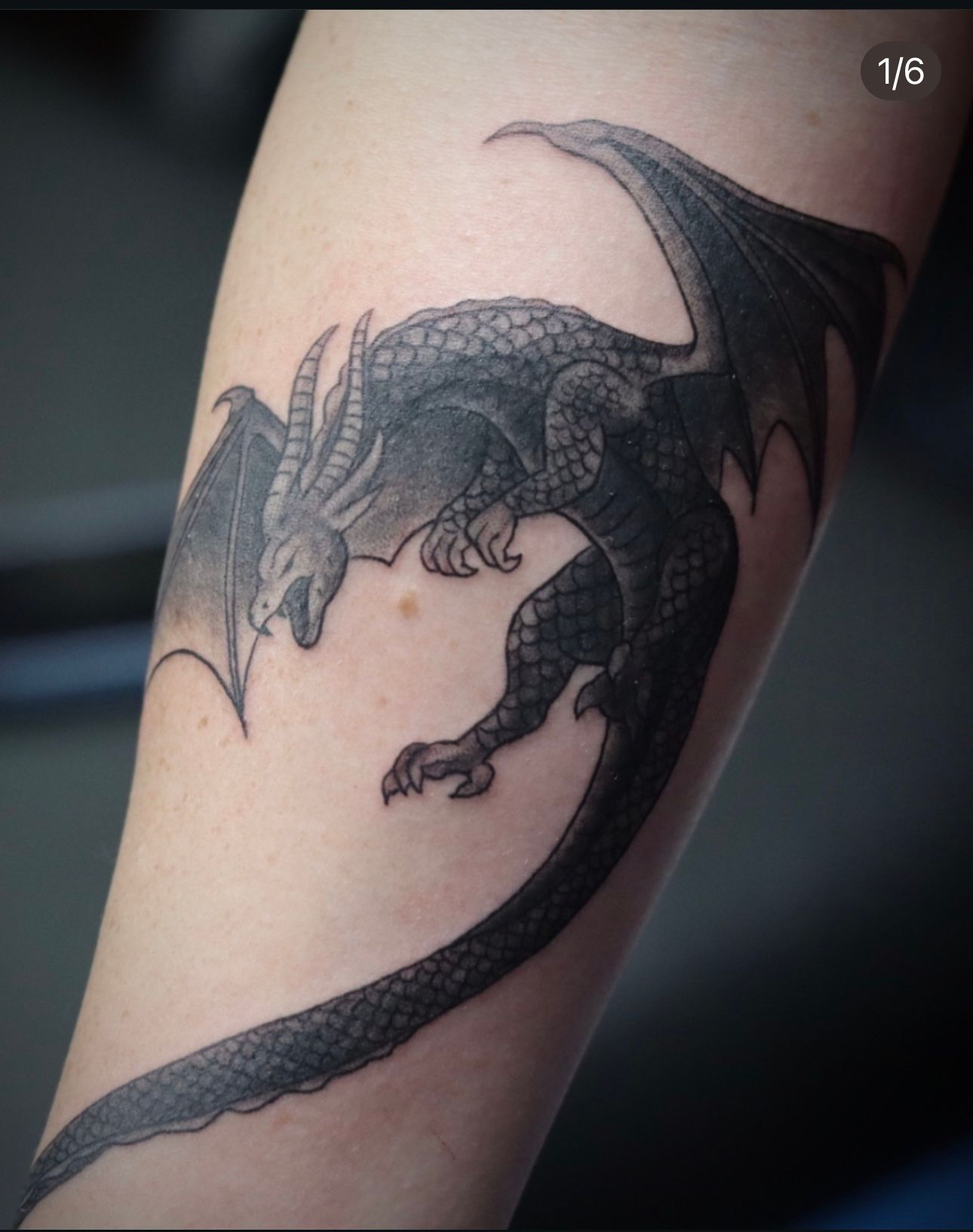 A black and white tattoo of a dragon on a person 's arm