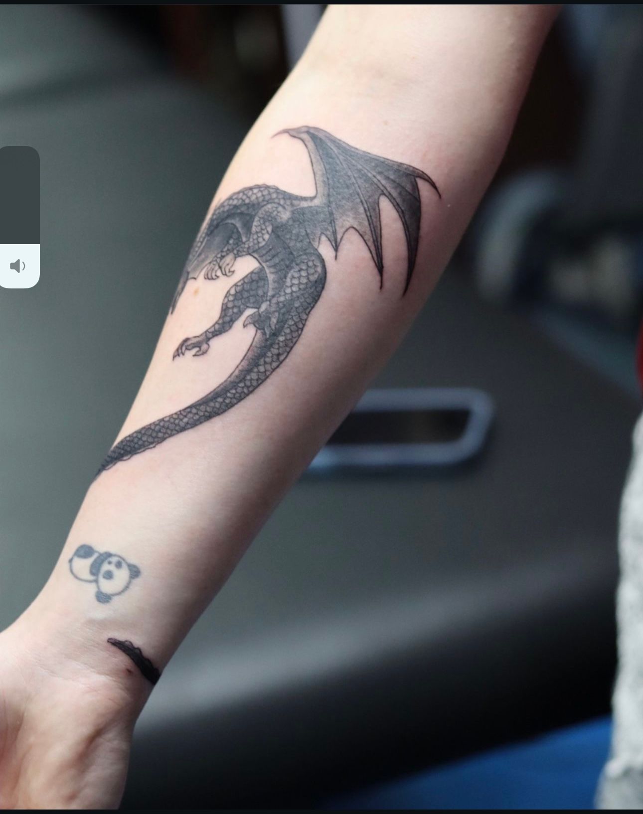 A person has a tattoo of a dragon on their forearm