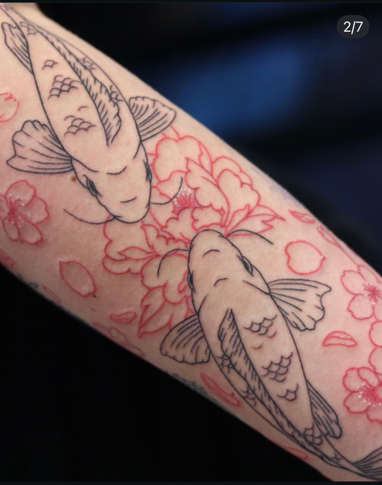 A tattoo of two fish and flowers on a person 's arm
