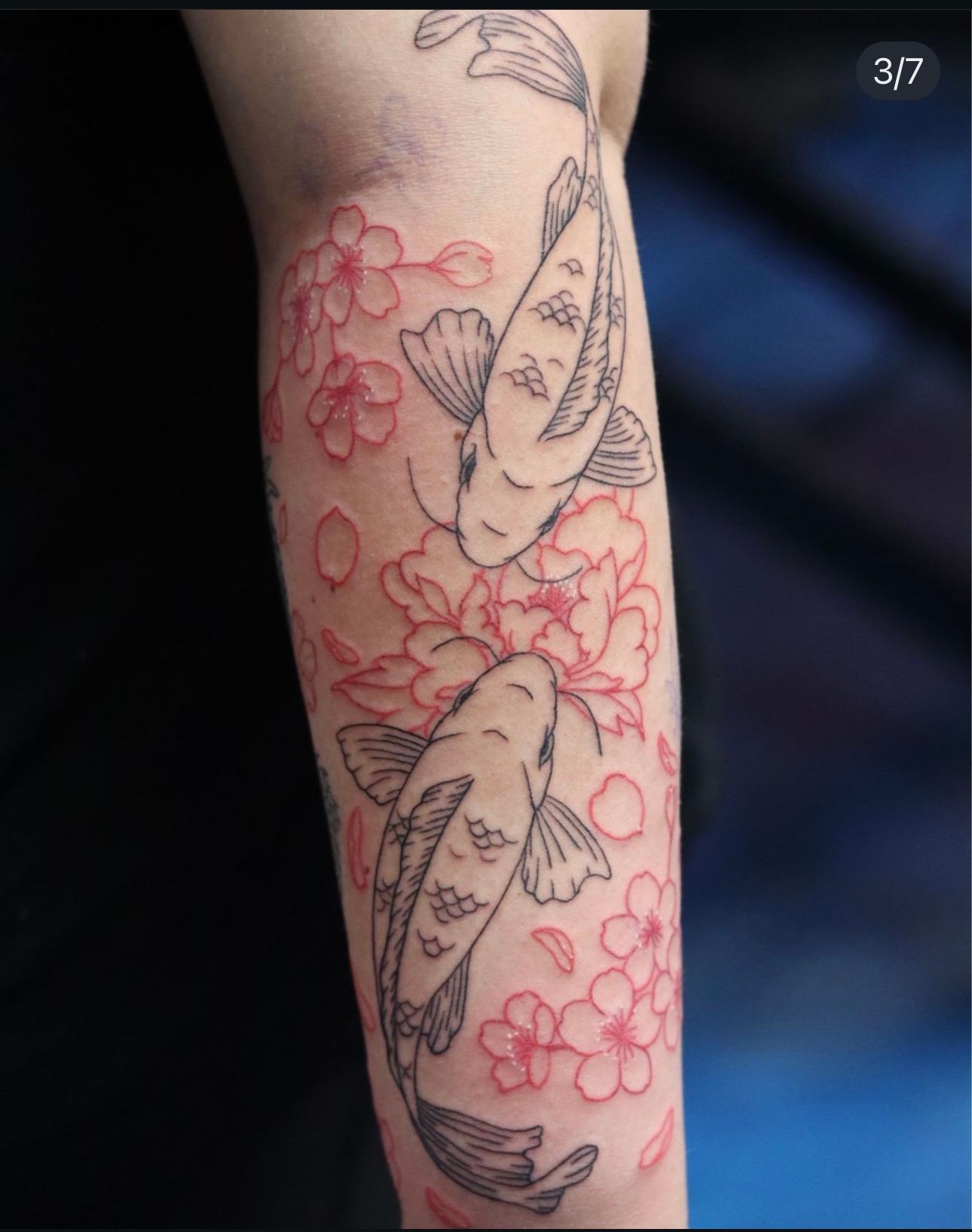 A tattoo of two fish and flowers on a person 's arm