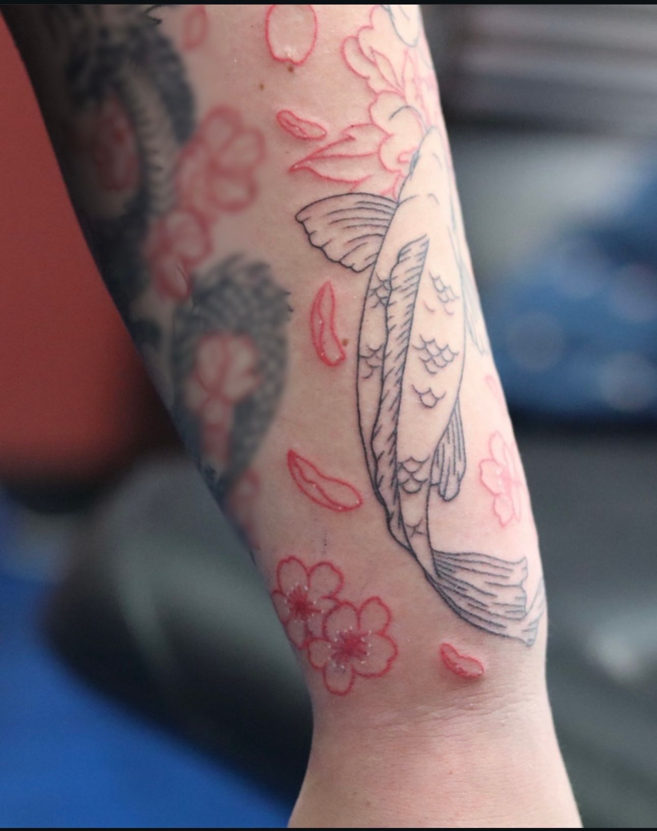 A person has a tattoo of a fish and flowers on their arm