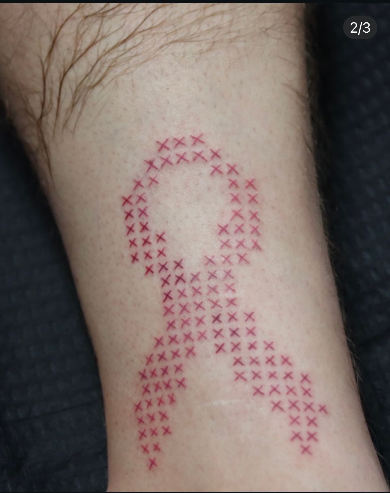 A person has a cross stitched ribbon tattoo on their leg