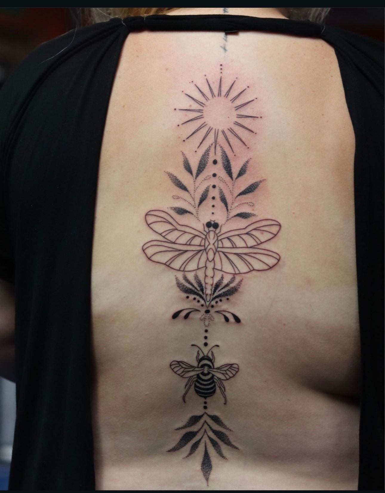 A woman has a tattoo of a bee and a dragonfly on her back