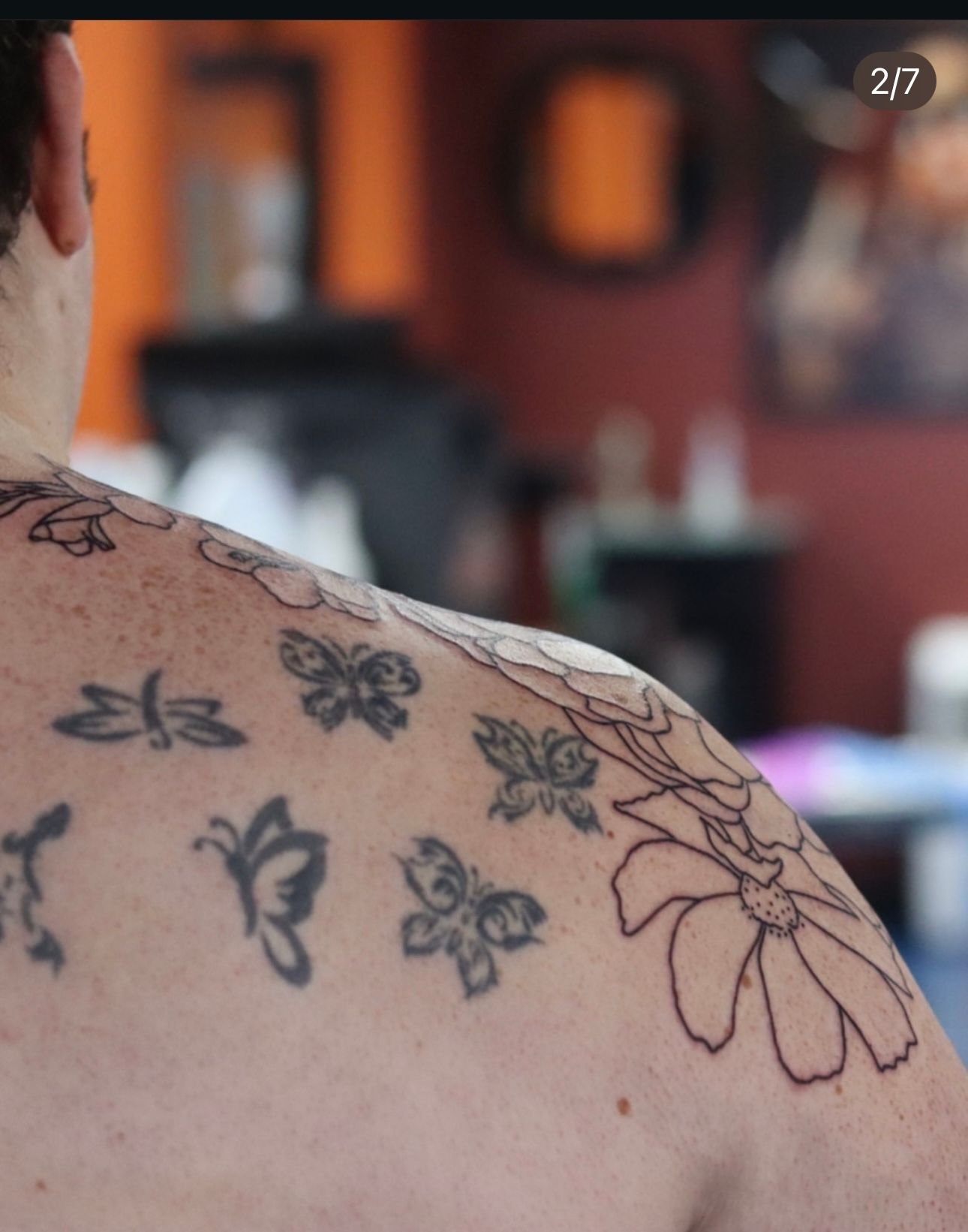 A man has a lot of tattoos on his back including butterflies and flowers