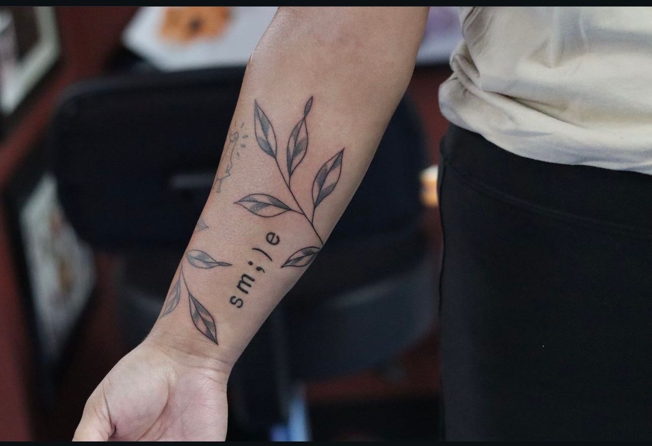 A person has a tattoo on their forearm that says smile