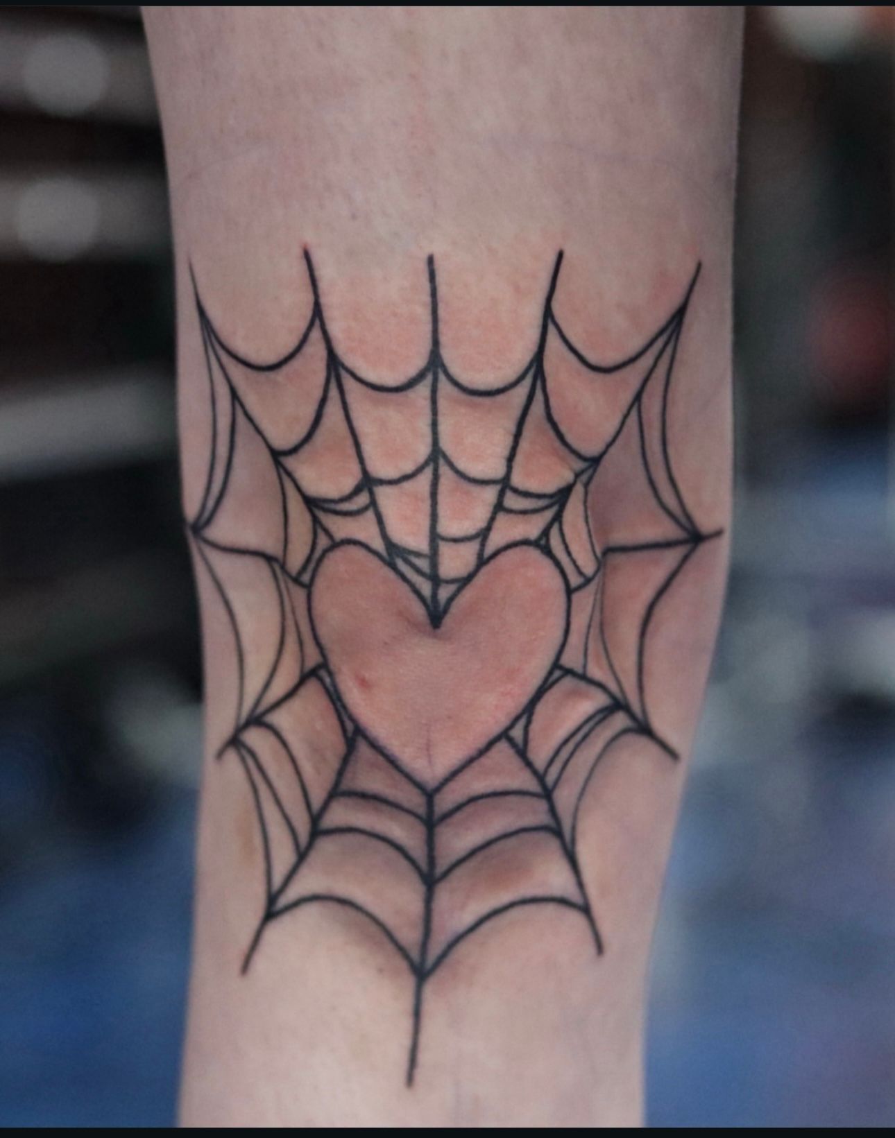 A tattoo of a spider web with a heart in it