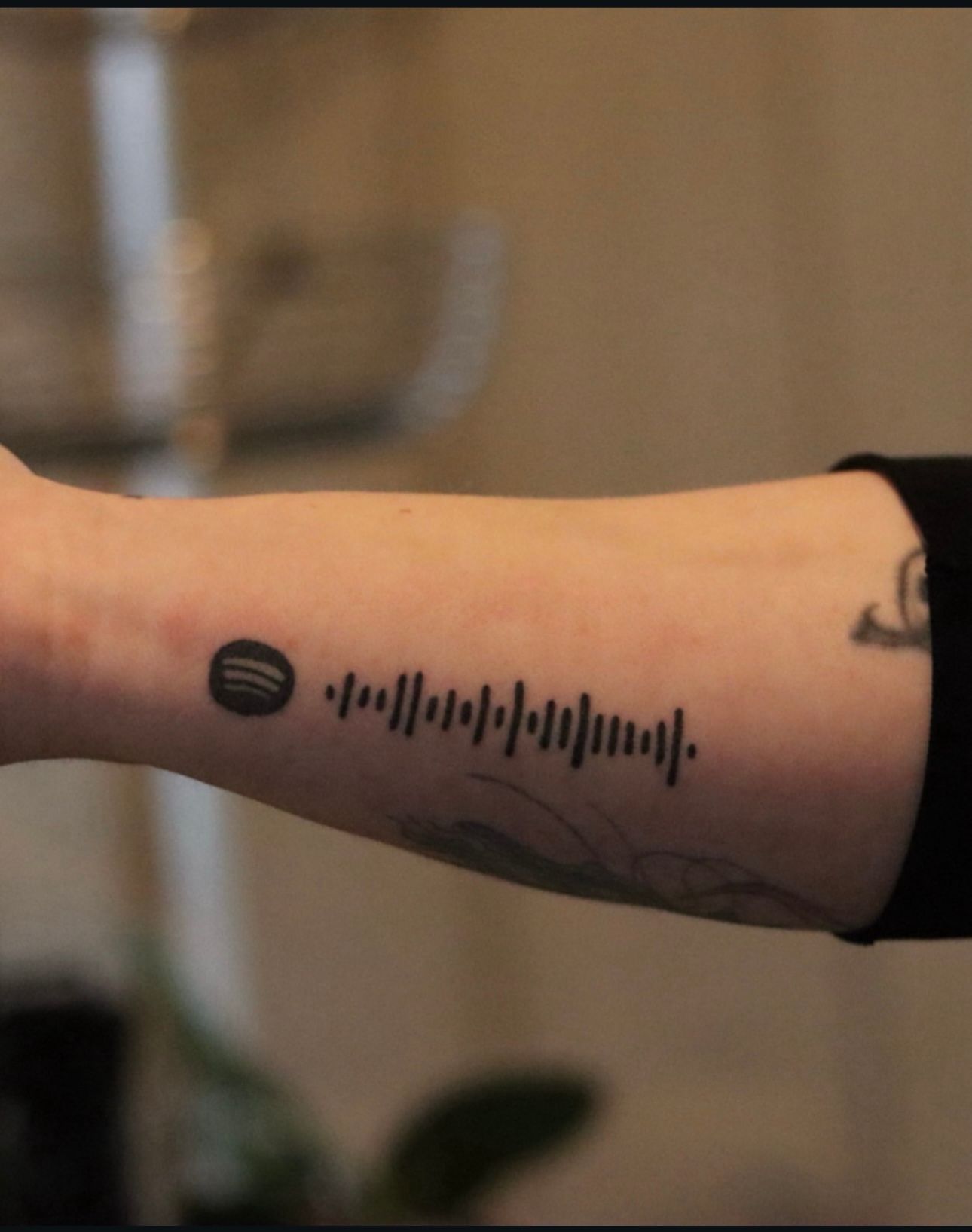 A person has a spotify tattoo on their forearm