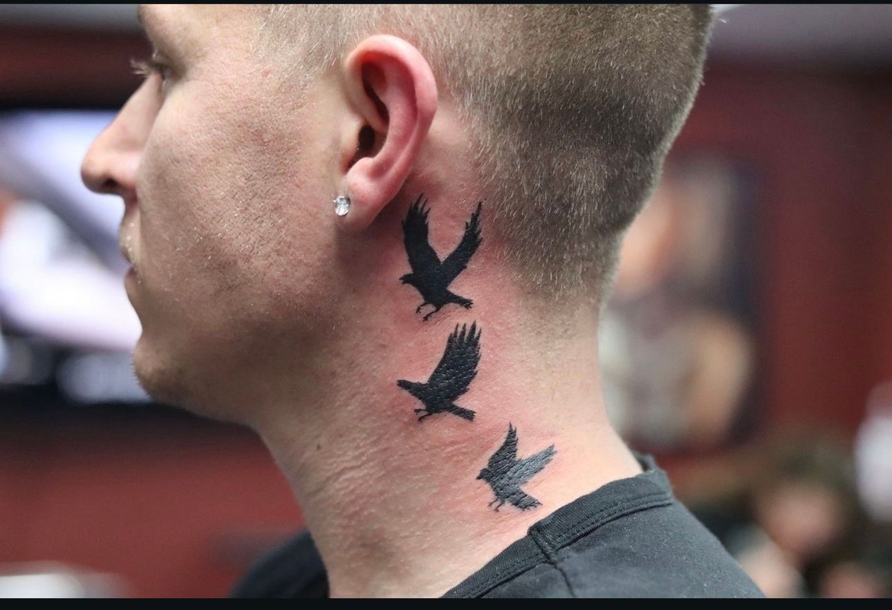 A man has three black birds tattooed on his neck