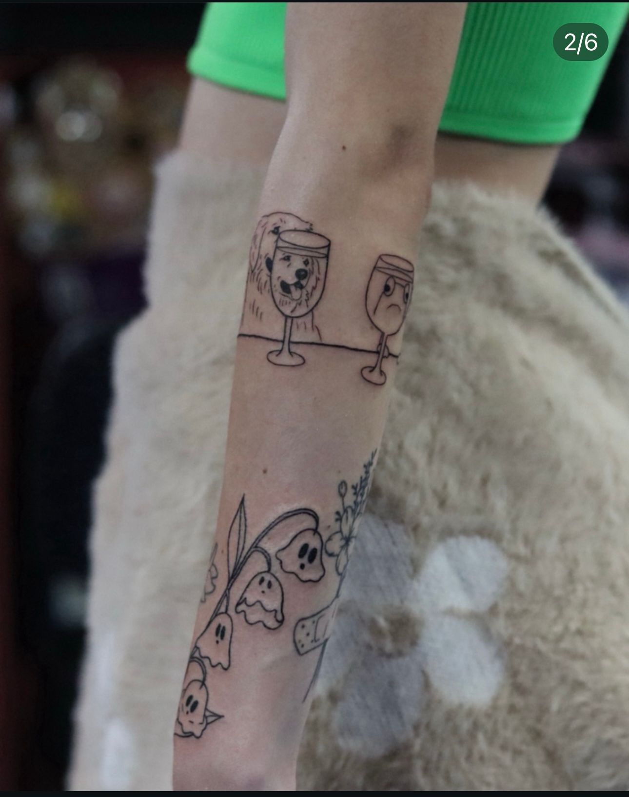 A woman has a tattoo of wine glasses and flowers on her arm