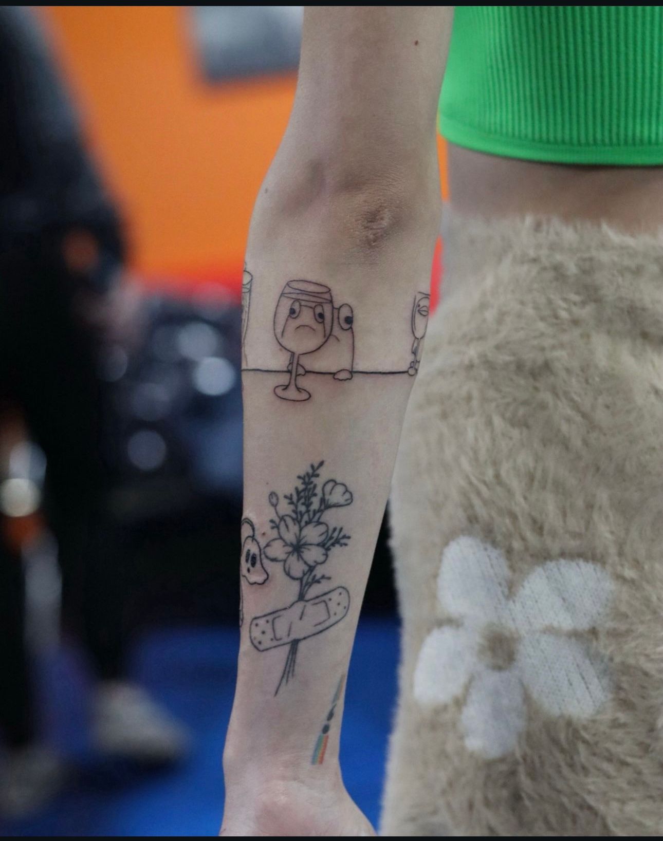 A woman has a tattoo of a wine glass and flowers on her arm