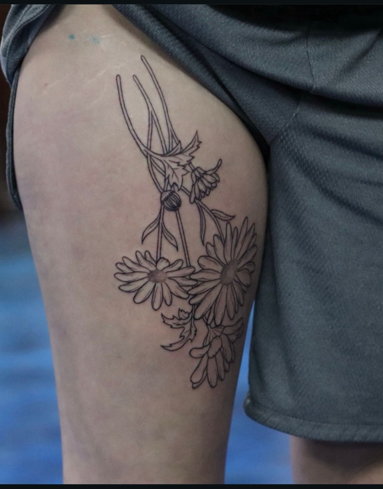 A woman has a tattoo of daisies on her thigh