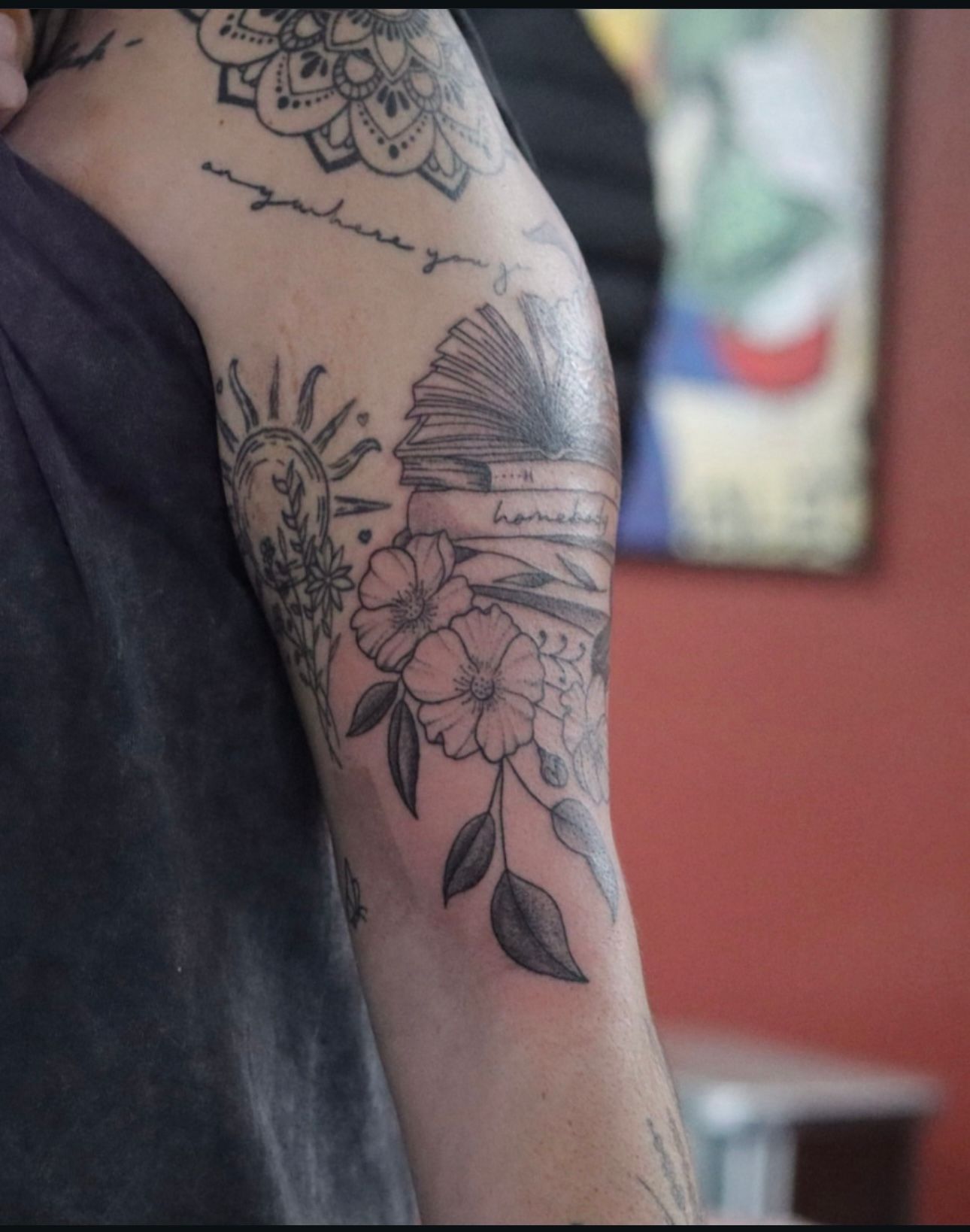 A man has a tattoo of a book and flowers on his arm