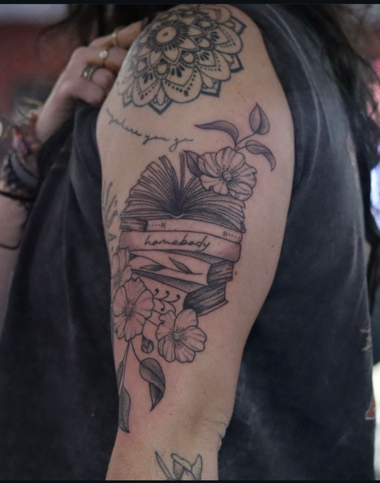 A woman has a tattoo of a book and flowers on her arm