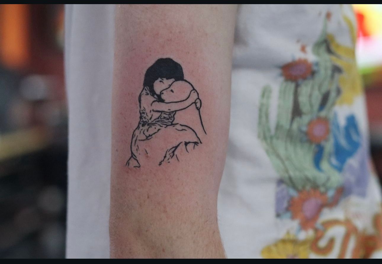 A woman has a tattoo of two people hugging on her arm