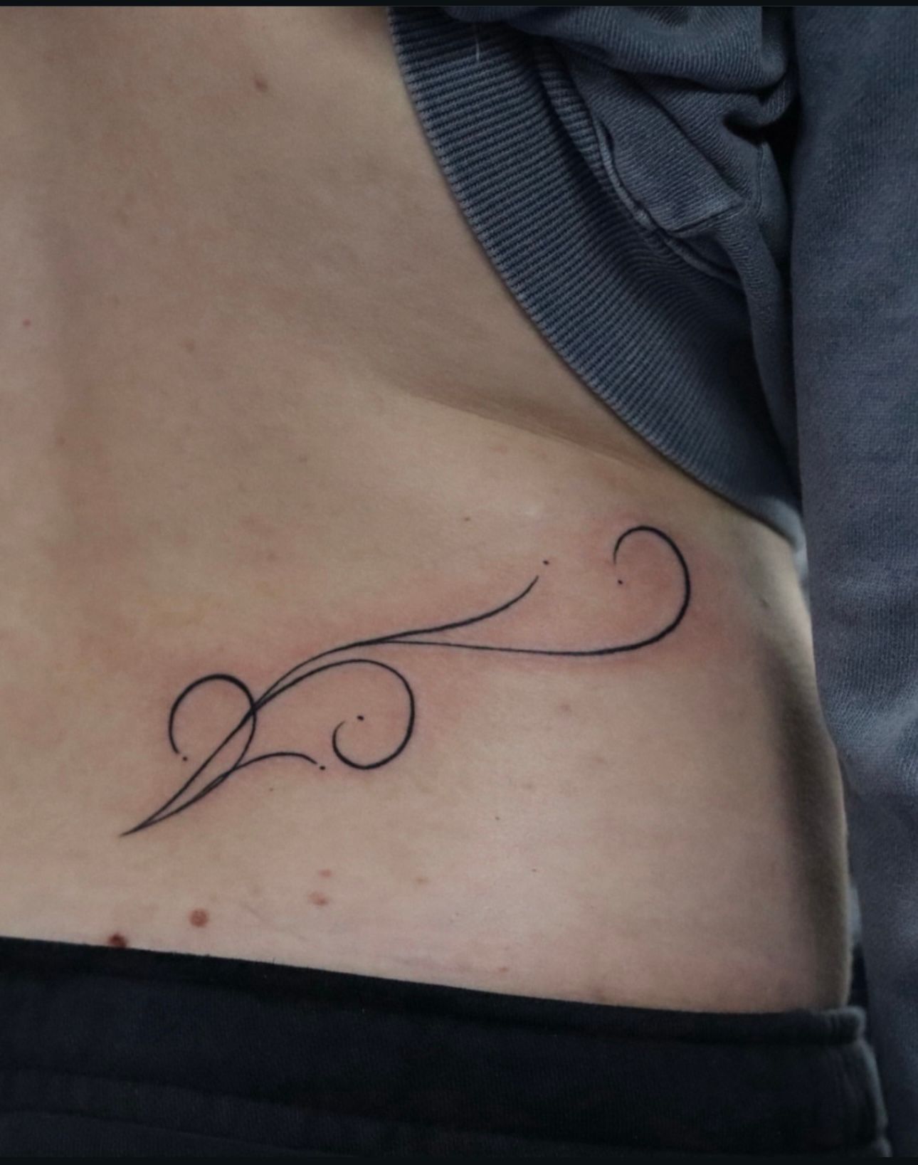 A person has a tattoo on their lower back that looks like a swirl