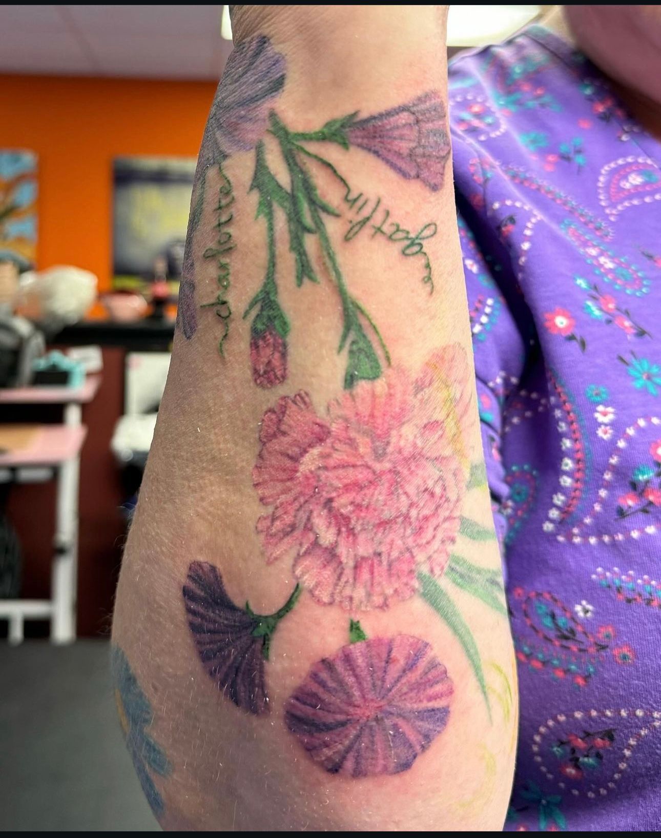 A woman has a tattoo of pink and purple flowers on her arm.