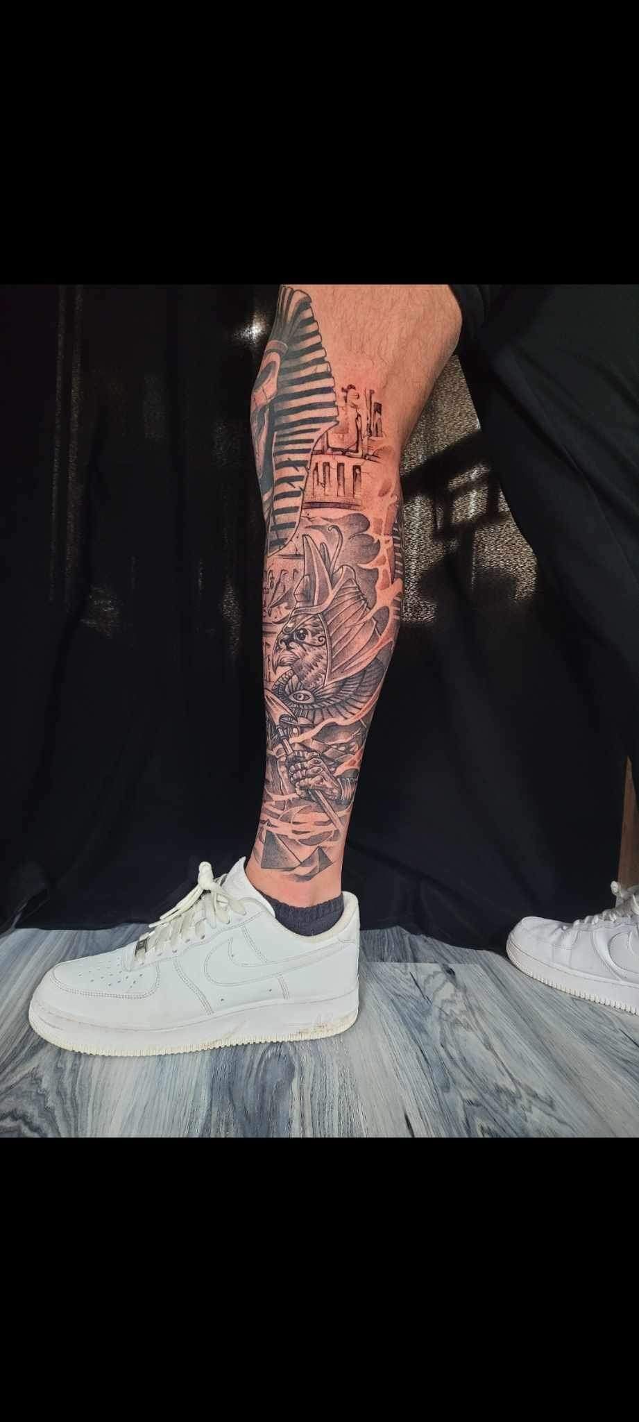 A person with a tattoo on their leg is wearing white sneakers.