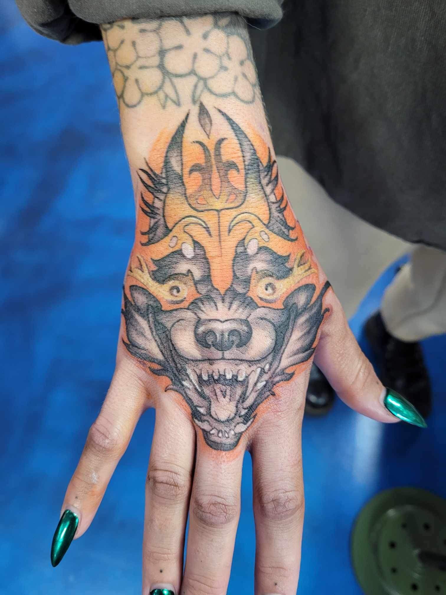 A woman has a tattoo of a wolf on her hand.