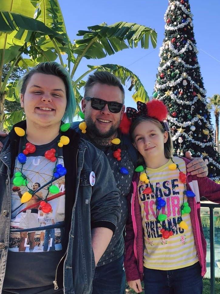 A man and two children are posing for a picture in front of a christmas tree.