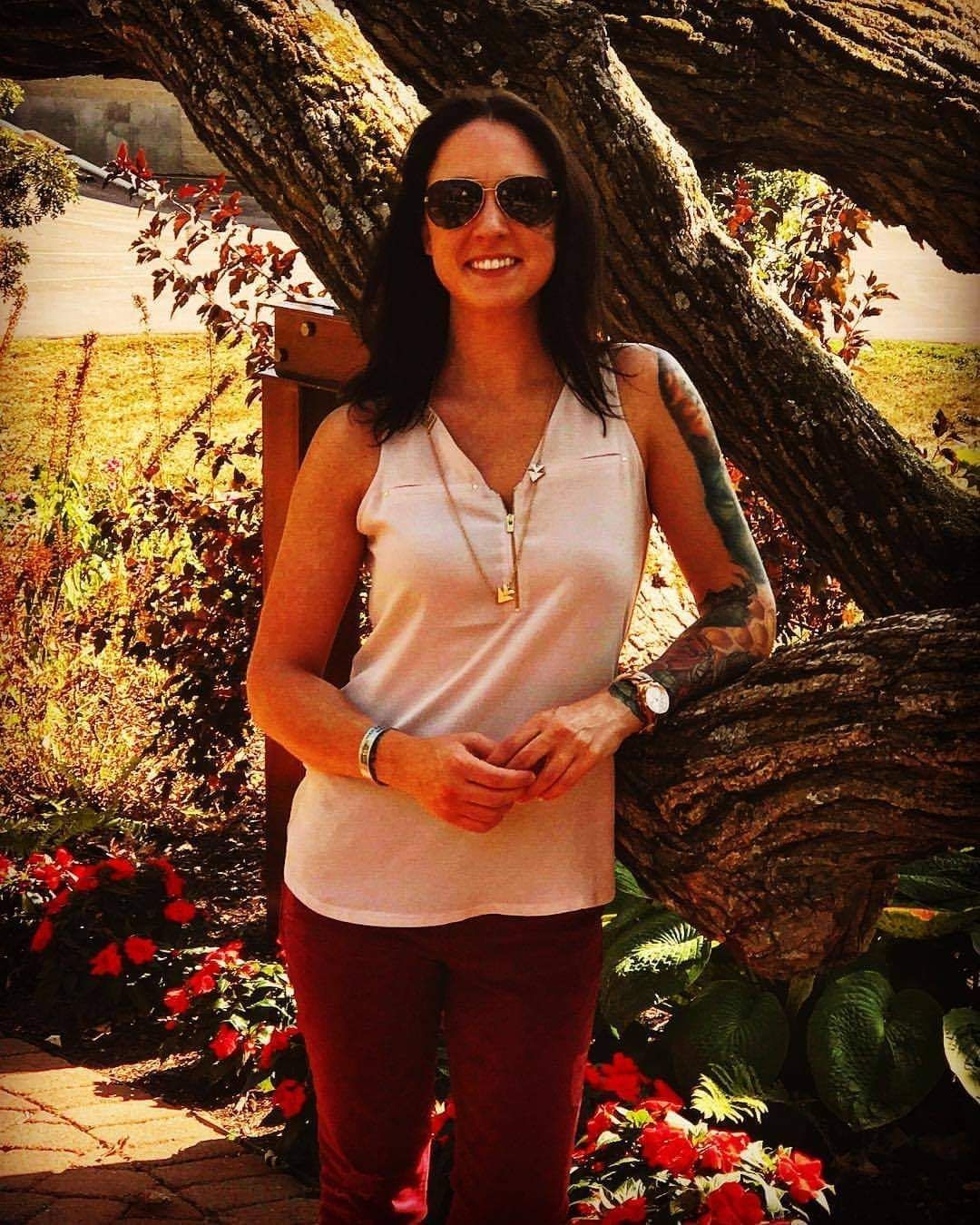 A woman wearing sunglasses is standing next to a tree