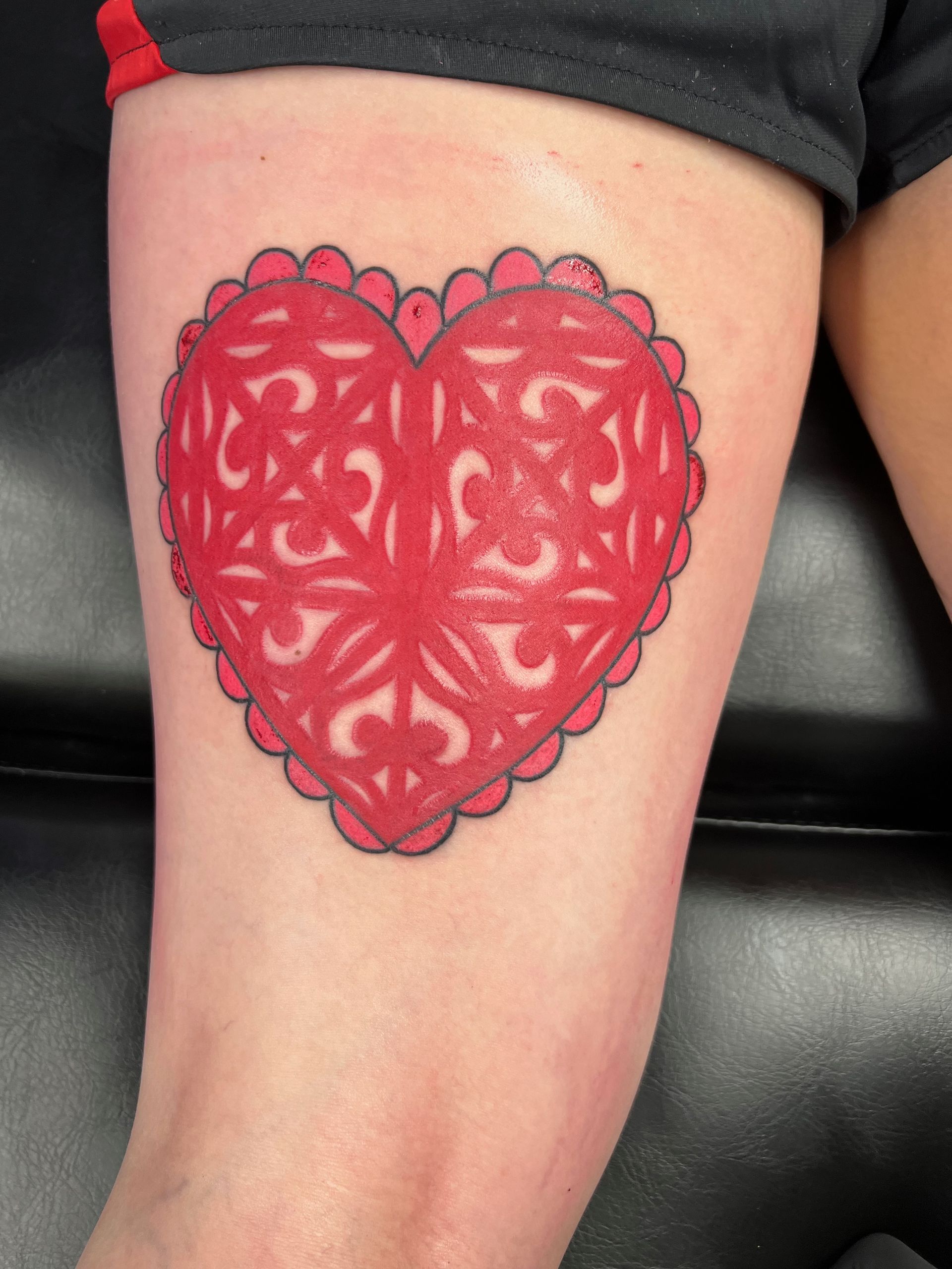 A person has a red heart tattoo on their leg