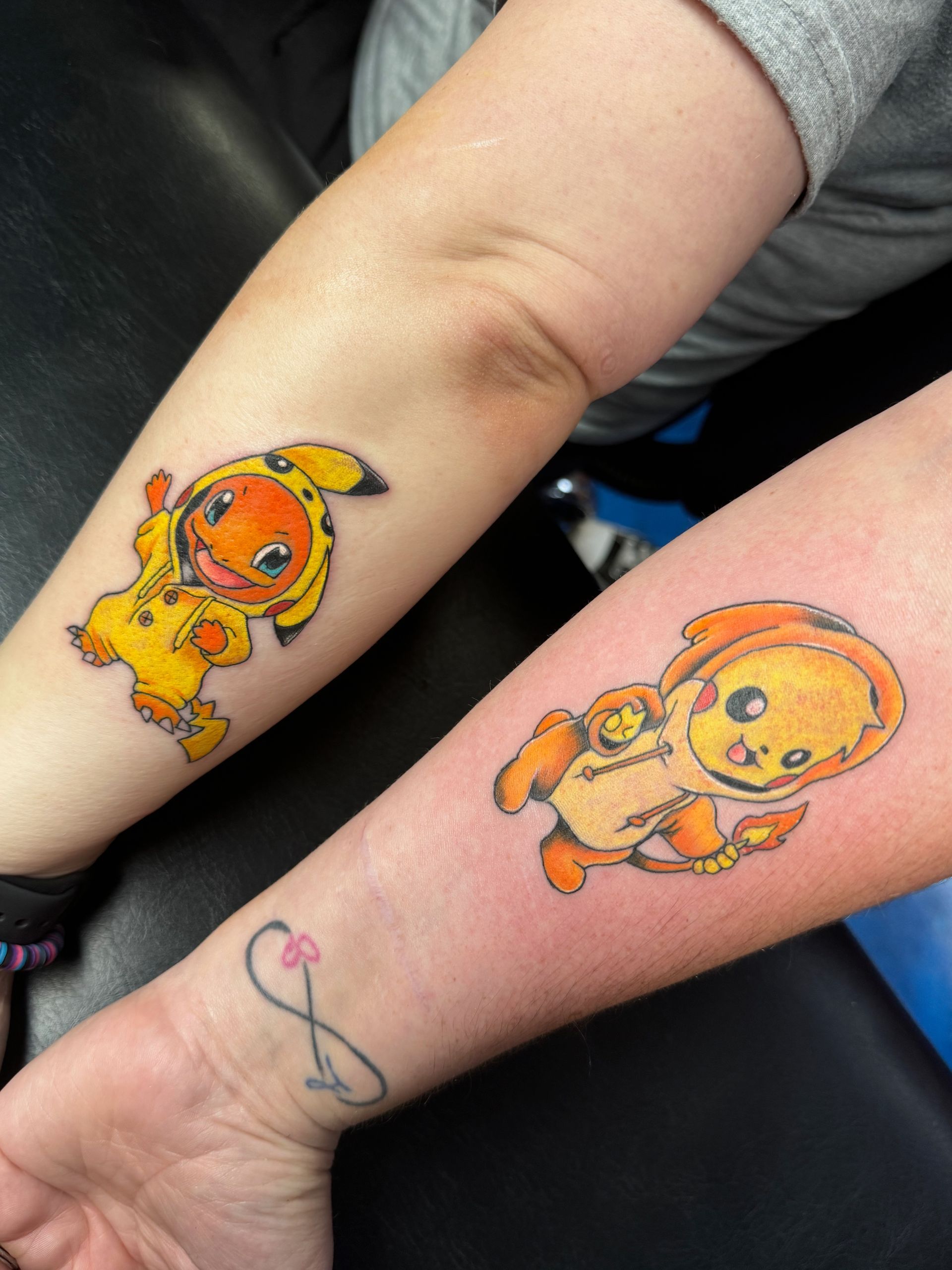Two people have matching tattoos of pikachu and charmander on their forearms