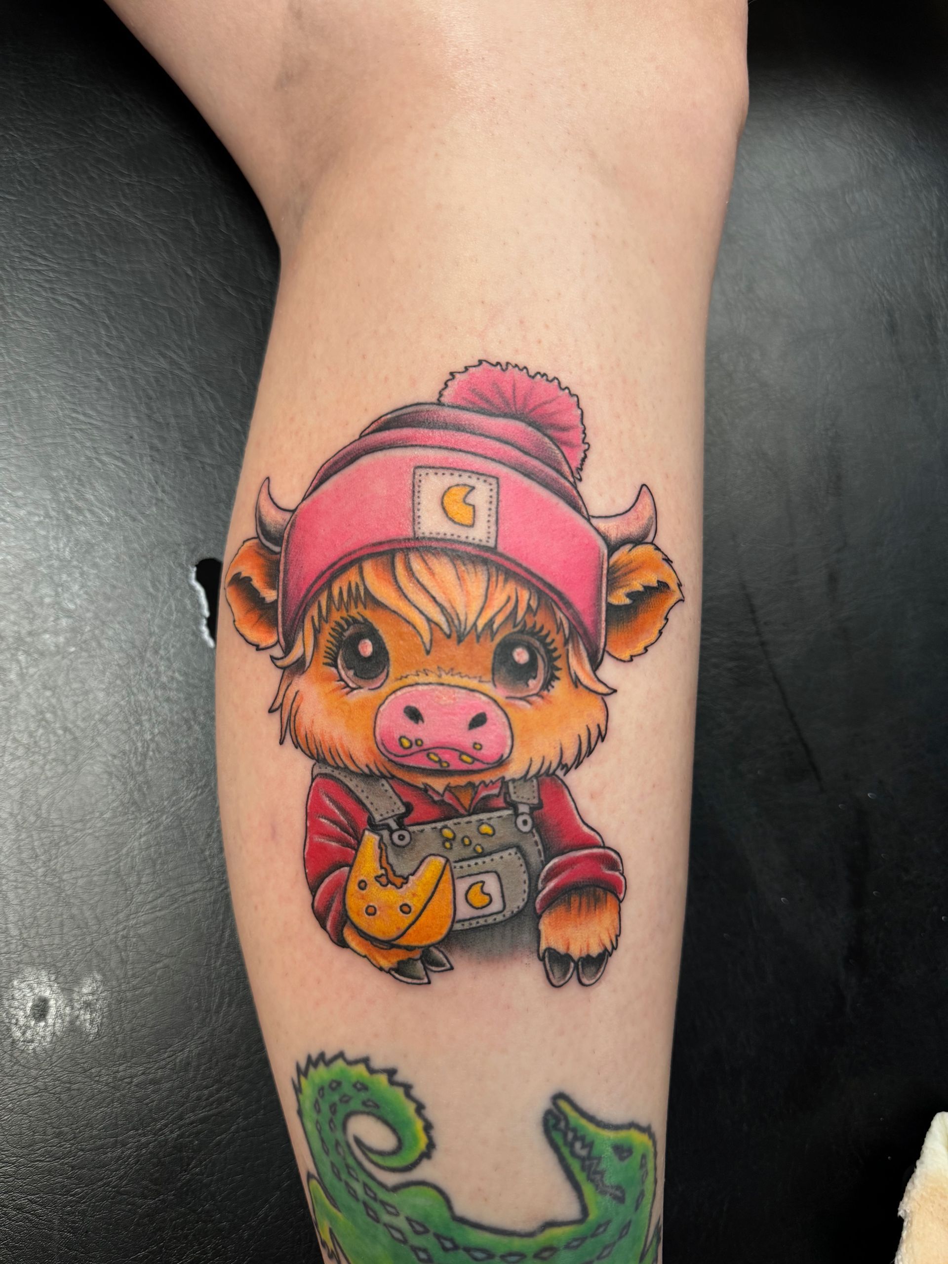 A tattoo of a cow wearing a pink hat and holding a camera