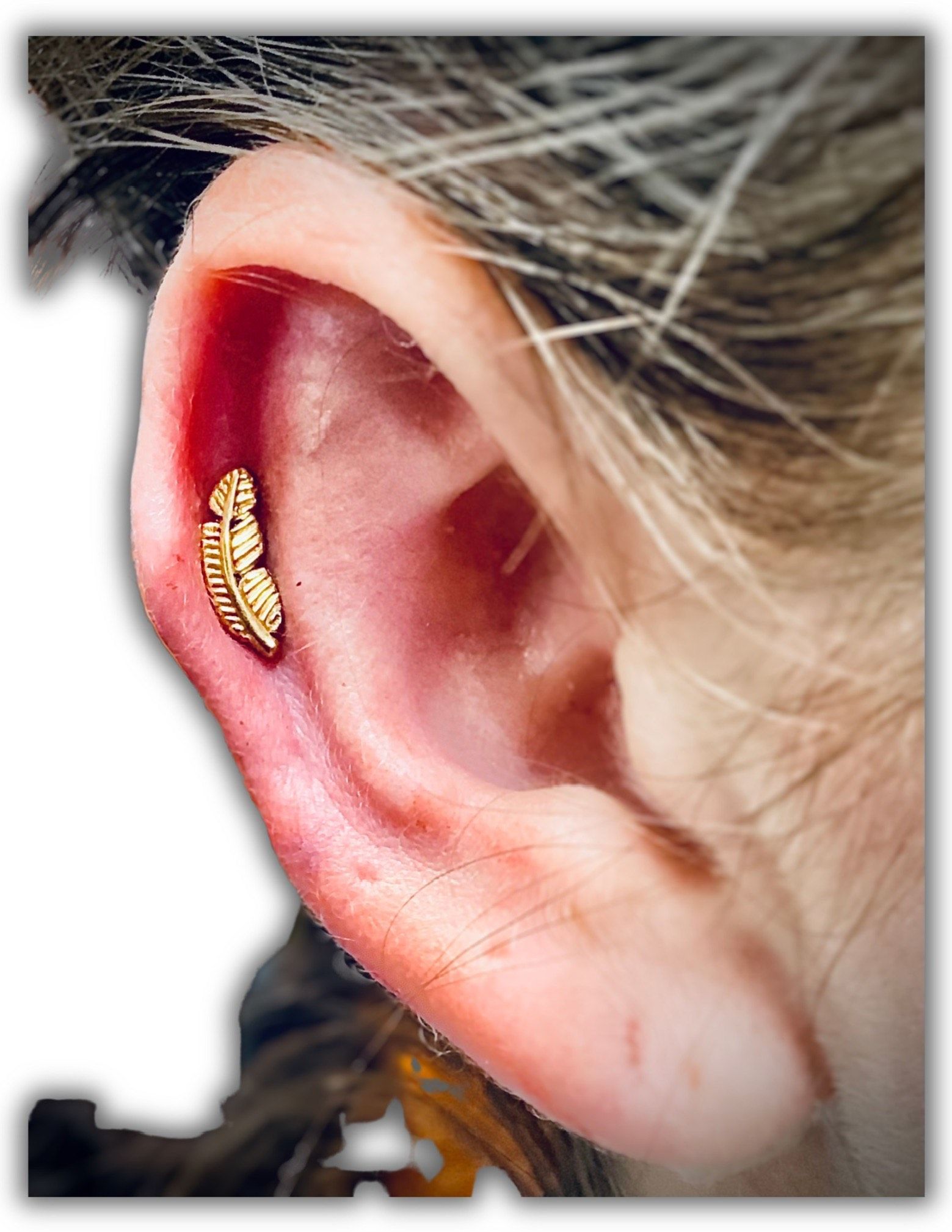 A close up of a person 's ear with a gold leaf piercing