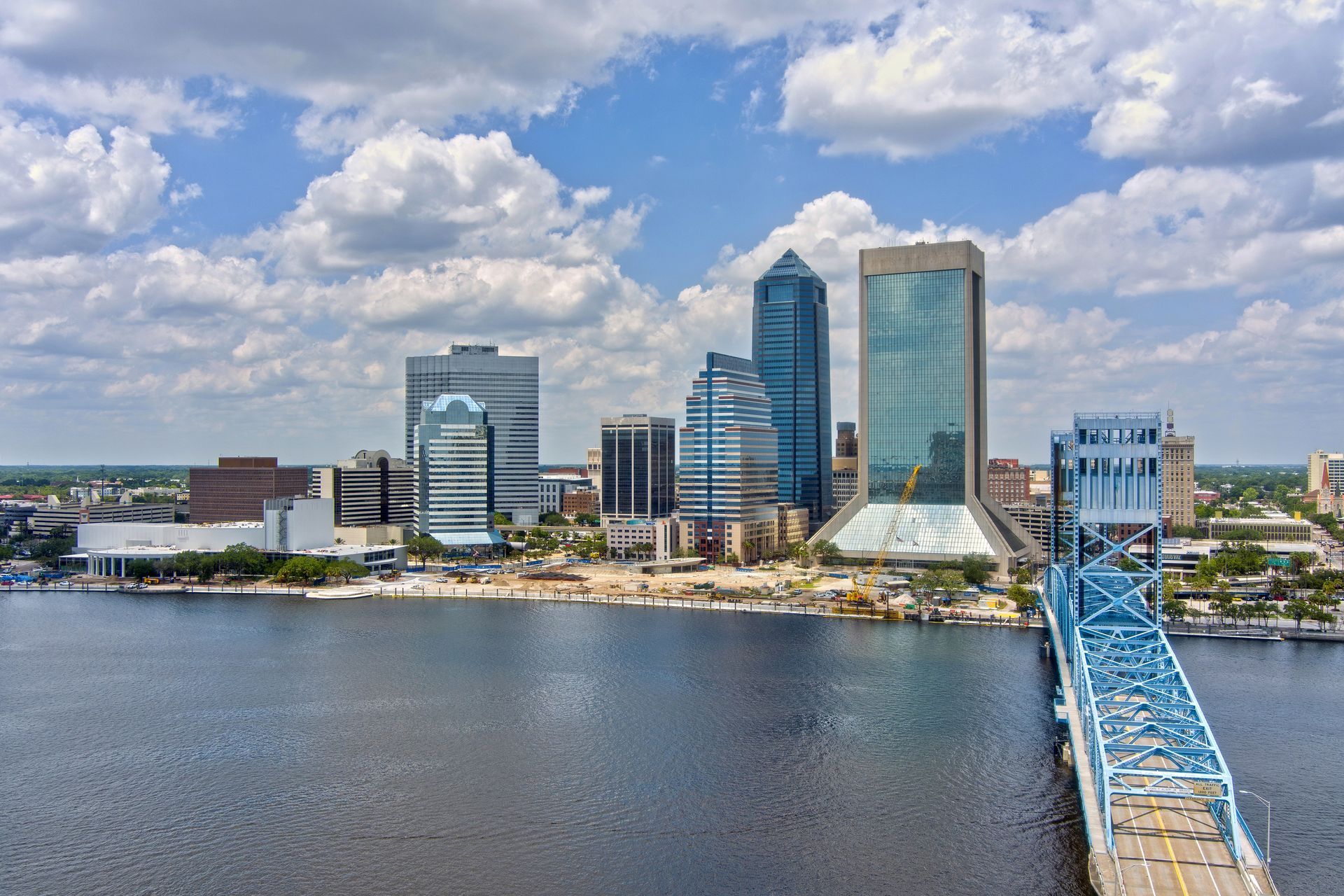 A view of the Jacksonville, Florida skyline across the St. Johns River, featuring the blue Main Street Bridge in front.